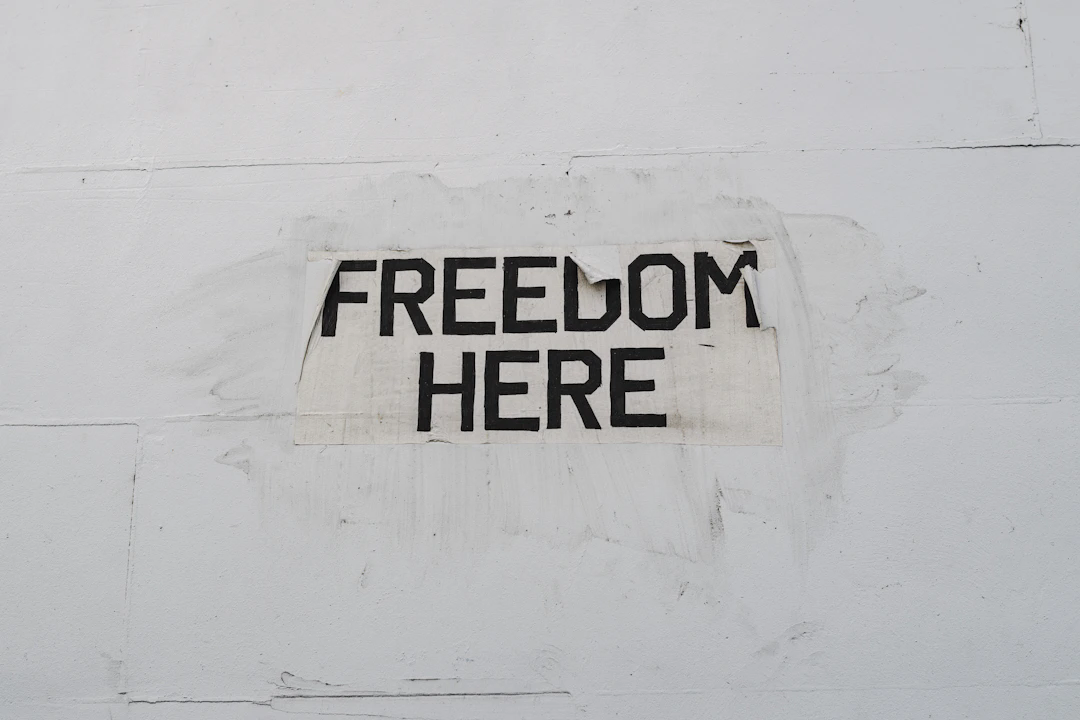 A white wall with a worn paper sign displaying the words 'FREEDOM HERE' in bold black letters.