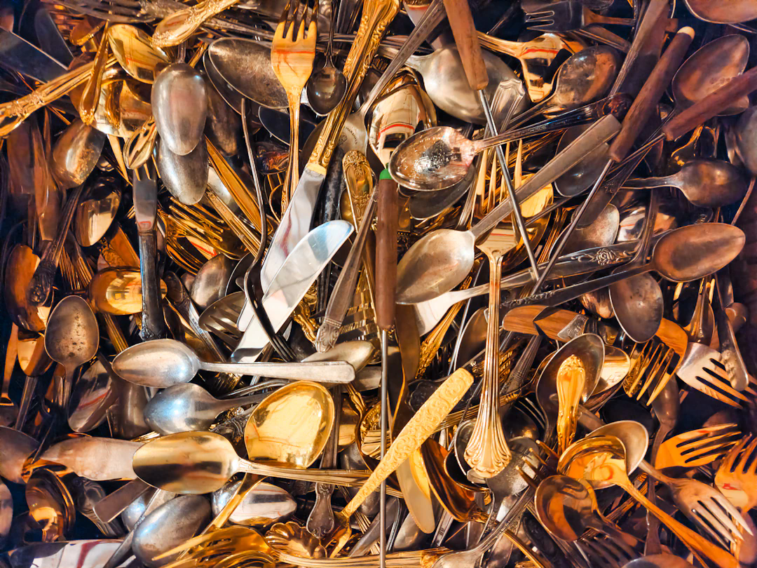 A large pile of assorted vintage cutlery including spoons, forks, and knives, some with decorative handles and a mix of silver and gold tones.