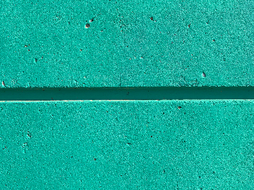 A close-up view of a turquoise-colored concrete wall with a horizontal groove running through the middle and small holes and texture variations visible.